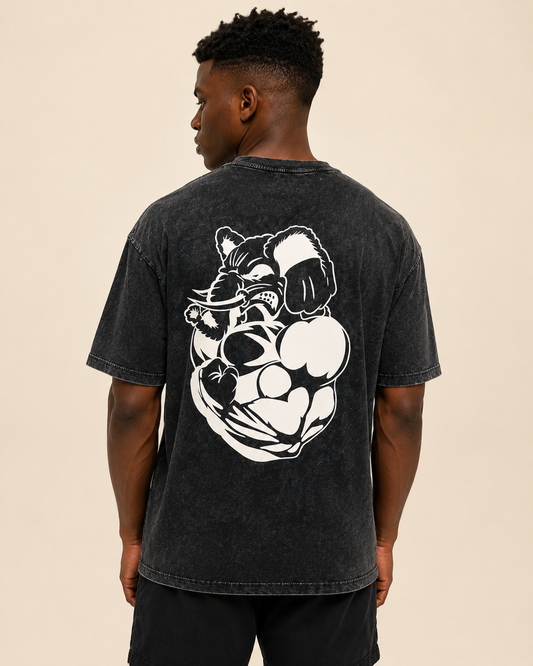 A man viewed from the back wearing a faded black graphic t-shirt with a large white muscular bear design on the back, set against a solid beige background.